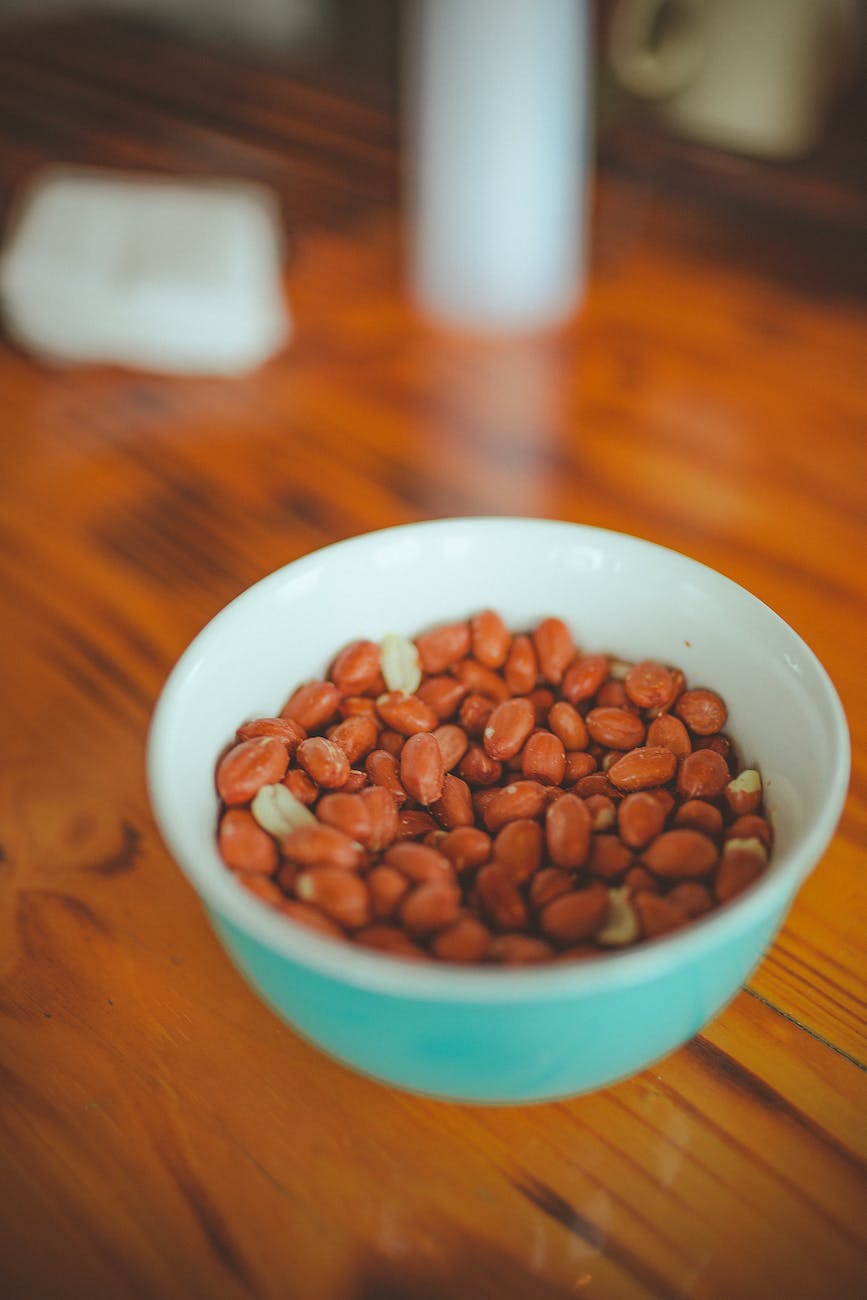 close up photo of a bowl full of roasted groundnuts on brown wooden table