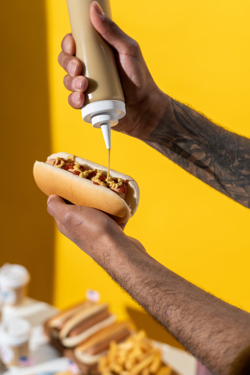 person putting mustard on hotdog