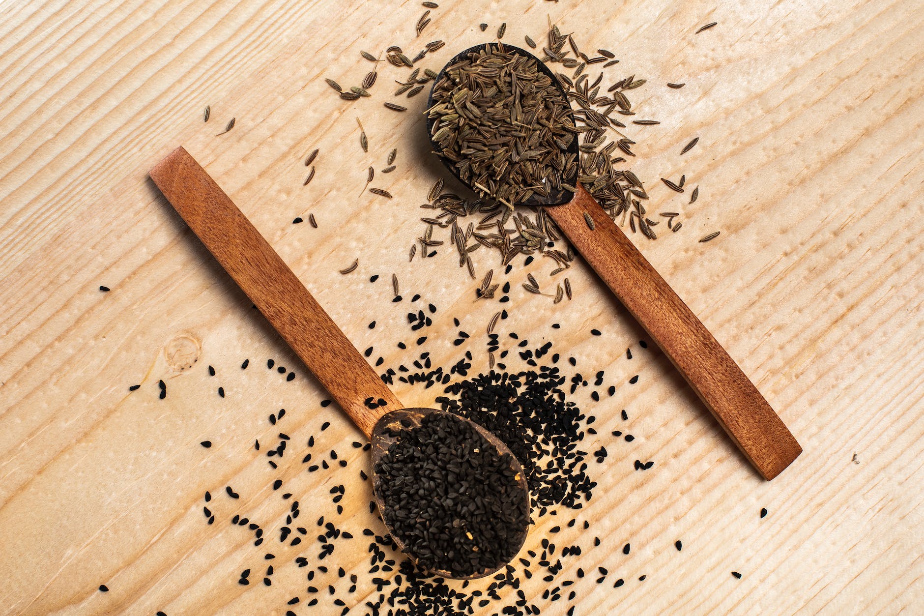 black sesame seeds and caraway seeds on wooden spoons
