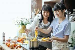 happy asian women cooking oriental noodles in kitchen